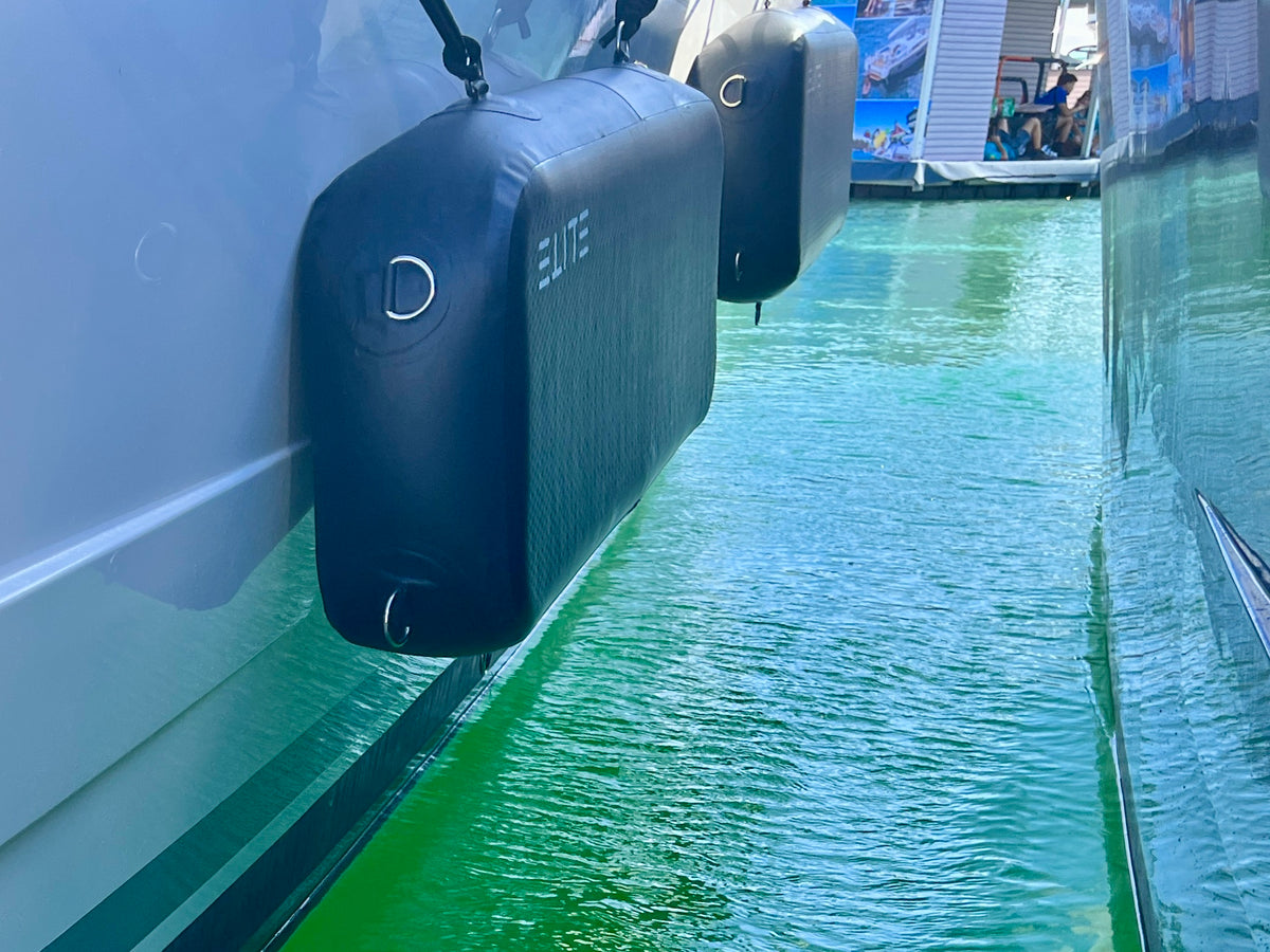 Two ELITE Sentinel flat fenders hanging beside a white yacht above clear turquoise water.