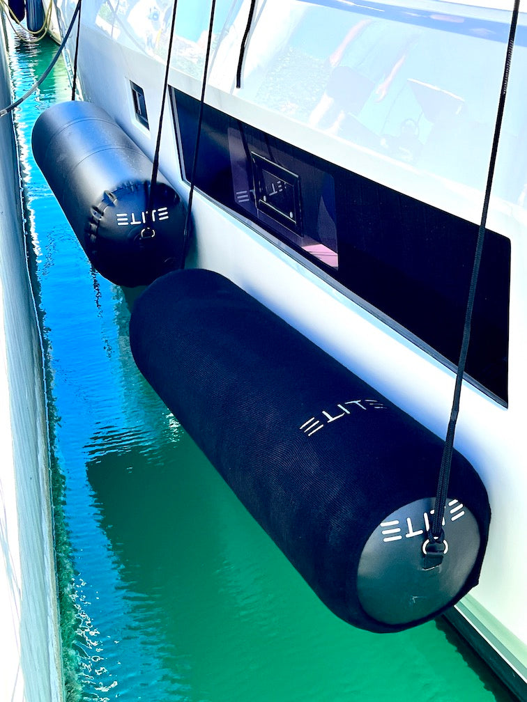 Covered ELITE cylindrical fenders suspended beside a yacht above turquoise water.