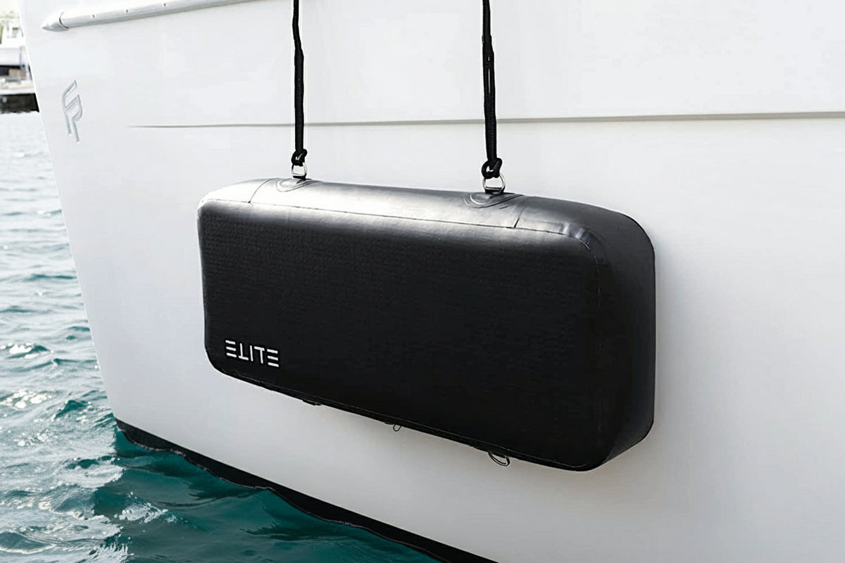 An ELITE Sentinel flat fender suspended horizontally against a white yacht above teal water.